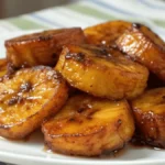Sweet plantain slices glazed in caramelized syrup on a white plate, perfect for sweet plantain recipes