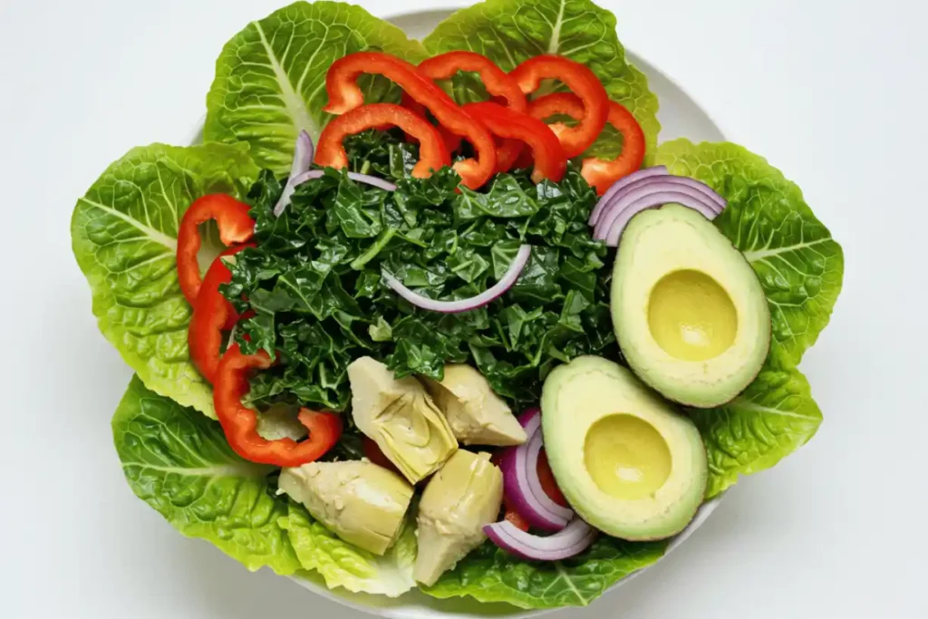 Fresh romaine lettuce, Tuscan kale, red bell peppers, red onion, avocado, and marinated artichoke hearts in a white bowl