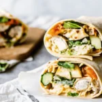 Chicken Caesar Wrap cut in half showing grilled chicken, greens, avocado, and creamy dressing inside a soft tortilla