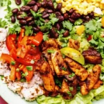 Colorful fajita chicken bowl with grilled chicken, rice, beans, guacamole, and fresh toppings on a plate