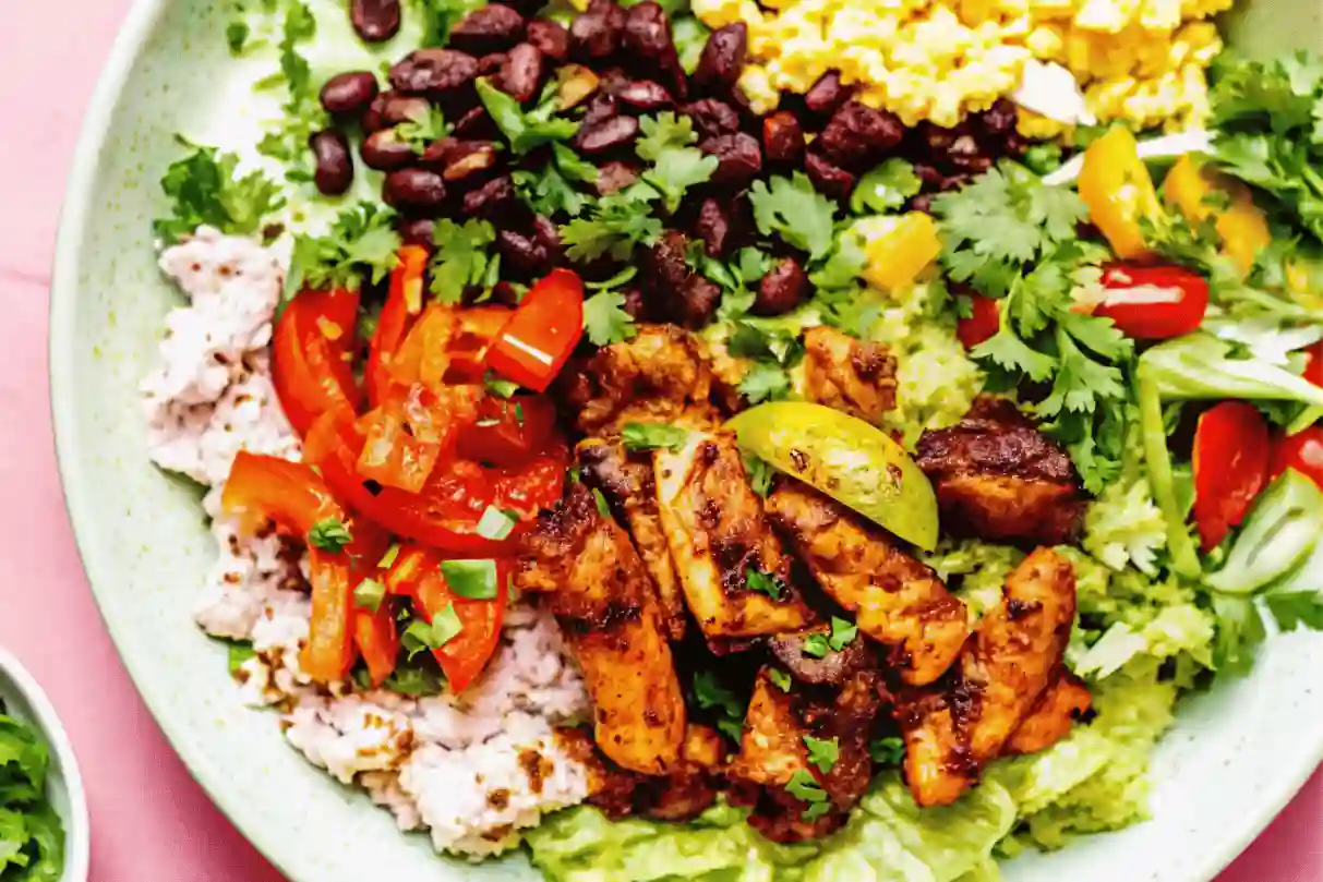 Colorful fajita chicken bowl with grilled chicken, rice, beans, guacamole, and fresh toppings on a plate