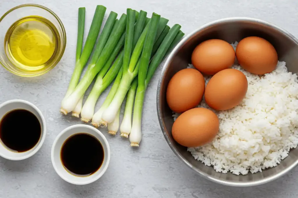 Basic arroz frito ingredients including green onions, eggs, cold rice, soy sauce, and oil arranged on a light background