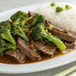 Chinese beef and broccoli with tender slices of beef, bright green broccoli, and glossy brown sauce served with white rice on a white plate