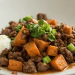 Plated ground beef and sweet potato cubes topped with fresh cilantro and green onions, served with sour cream