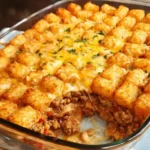 Golden Cheesy Beef Bacon Cheeseburger Tater Tot Casserole in a white baking dish topped with crispy tater tots and parsley.